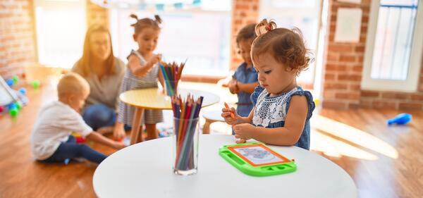 Beautiful teacher and group of toddlers playing around lots of toys at kindergarten